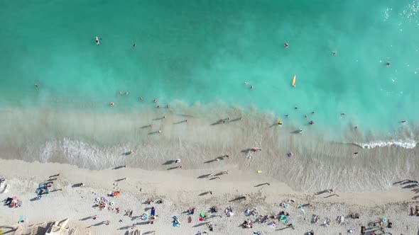 Overhead aerial of crystal clear blue waters as waves crash and people on vacation enjoy family time