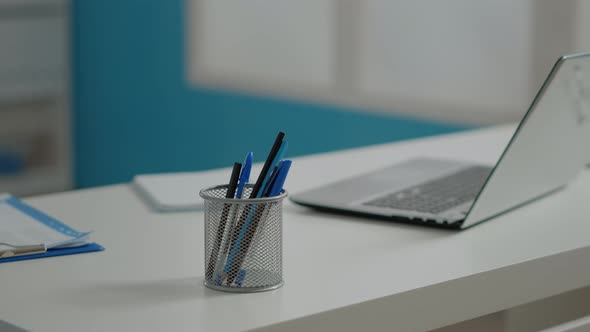 Close Up of Pens and Laptop on White Desk in Empty Cabinet