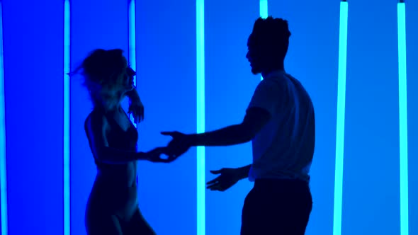 Dancers Practice a Series of Spins Against a Backdrop of Bright Blue Neon Lights in a Dark Studio