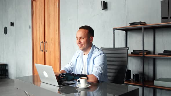 Smiling man programmer with artificial bio hand prothesis types on laptop keyboard