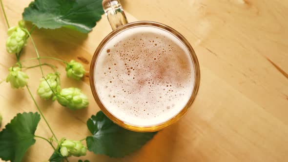 Top View of Mug of Beer with Foam and Hops on Bright Wooden Table