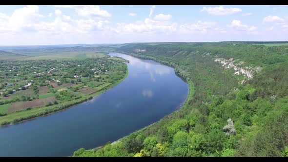 A wide blue river flows between rocks with trees and countryside with long fields