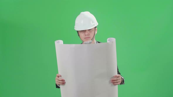 Asian Chief Engineer In The Hard Hat Holding Blueprint And Walks On Green Screen Chroma Key