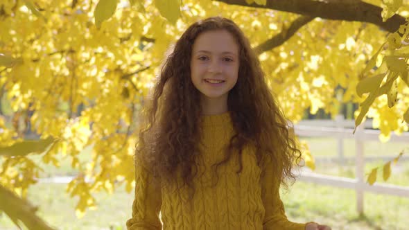 Portrait of a Cute Caucasian Girl with Long Curly Hair Smiling To the Camera on the Background