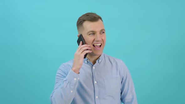 Caucasian Middleaged Man in a Blue Shirt Raises a Smartphone to His Ear and Talks