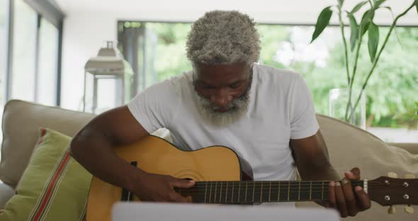 Video of sad african american senior man playing the guitar and using laptop