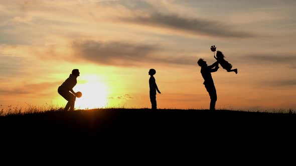 Family Vacation In Nature. Mom And Son Playing With The Ball. Dad Twists His Daughter In His Arms As