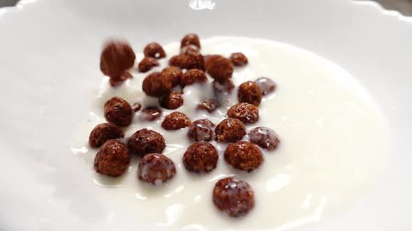 Close Up of Falling Chocolate Cereal Balls in Plate Full of Milk in Slow Motion