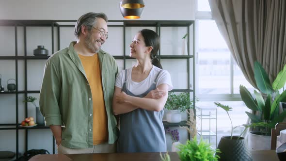 Asian mature couple sitting and smiling in living room. husband hand holdwife arm from behind