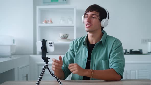 Young Man in Wireless Headphones is Talking on a Video Call Using His Mobile Phone