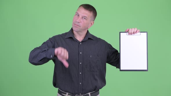 Stressed Macho Mature Businessman Showing Clipboard and Giving Thumbs Down