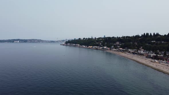 Drone shot revealing the Seattle skyline, including the Space Needle, from behind a hill near Alki b