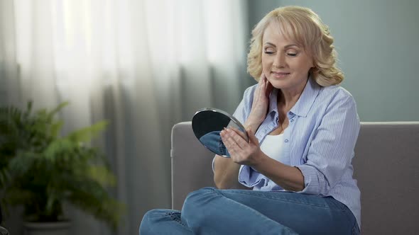 Mature Woman Looking Into a Hand Mirror, Enjoying Reflection. Anti-Age Cosmetics