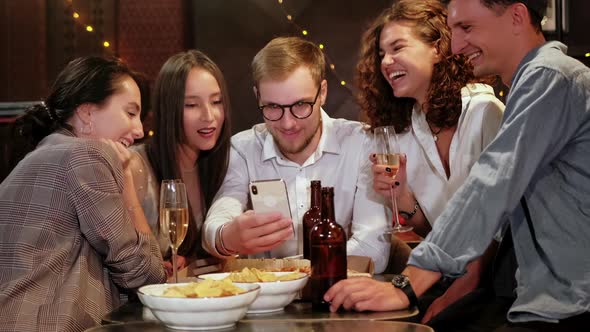 Company of Focused Hipster Friends Using Smart Phone in the Bar, Pub While Caucasian Man Start