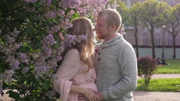 Pregnant Woman in a Pink Dress Walks with Her Husband. Married Couple Expecting a Baby on the