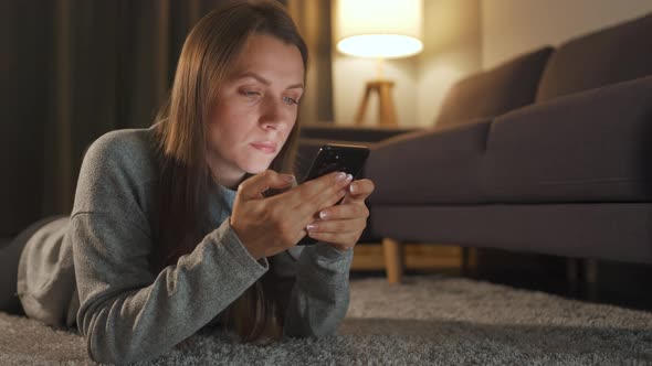 Woman Is Lying on the Floor and Using Smartphone in the Evening