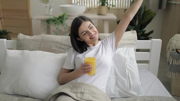 Cheerful Girl Drinking Orange Juice in Bed 