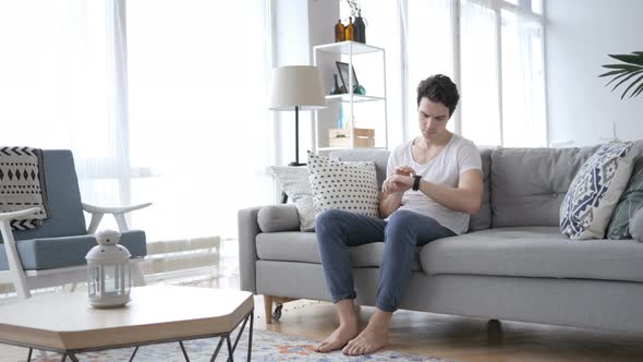 Young Man Using Smartwatch while Relaxing on Sofa