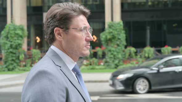 Middle Aged Businessman Walking on Street, Side View