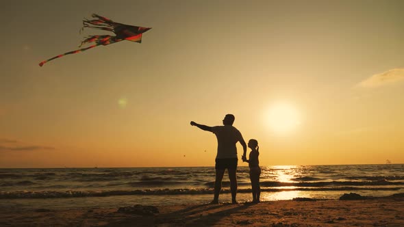 Happy Family Father and Child Daughter Launch a Kite on Beach at Sunset. Funny Family Time. Concept