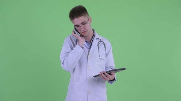 Happy Young Man Doctor Talking on the Phone While Using Digital Tablet