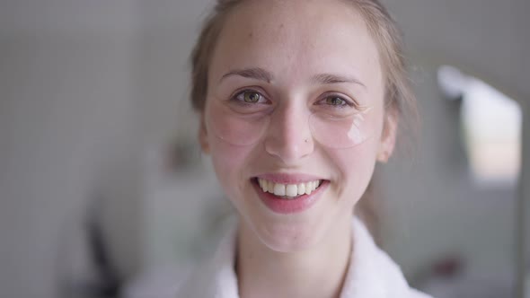 Closeup Face of Smiling Slim Beautiful Woman with Eye Patches Looking at Camera Standing in Bathroom