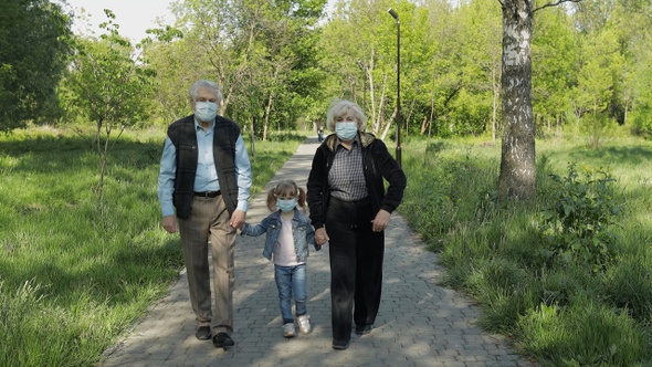 Old Grandparents with Granddaughter in Medical Masks Walk in Park. Coronavirus