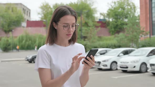 Young Woman Browsing Internet on Smartphone while Walking on Street