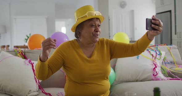 Happy african american senior woman holding champagne making new year's eve smartphone video call