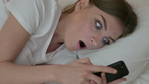 Portrait of Young Female Feeling Shocked Using Smartphone in Bed 