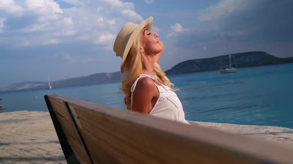 Woman in Sun Straw Hat Sitting on a Wooden Bench on Blue Sea Background at Ermioni