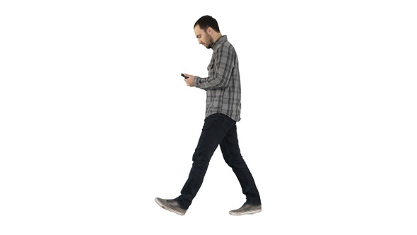 Young smart casual man walking and reading message on cell