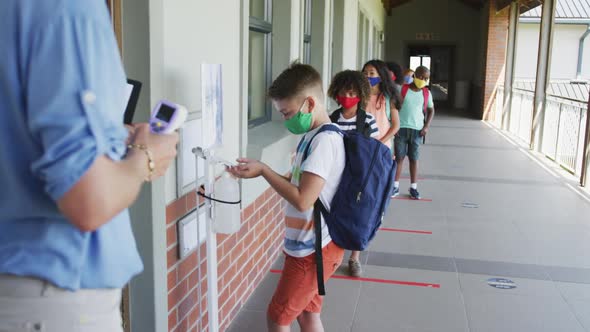 Boy wearing face mask sanitizing his hands at school