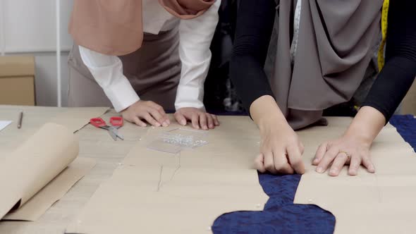 Muslim dressmaker pinning paper pattern on fabric at the table in tailor shop