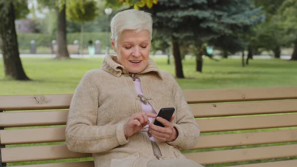 Overjoyed Grayhaired Mature Woman Sitting Outdoor Using Phone Browsing Smartphone Apps Looking at