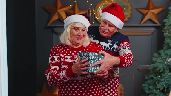 Grandfather Covering Eyes of Old Grandmother with Surprise Christmas Gift Present Box at Home Room