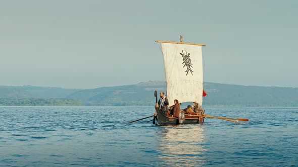 Vikings Sail on an Old Ship with a Raised Sail on a Calm River