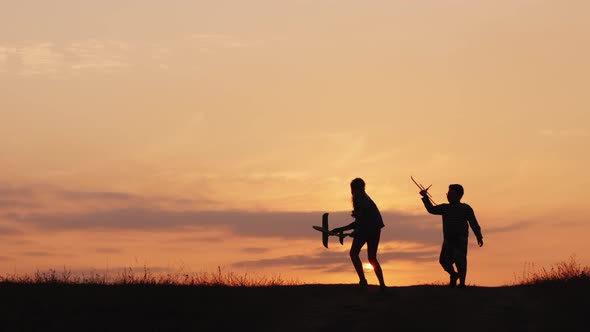 Silhouettes of a Girl and a Boy Playing Together with Airplanes at Sunset. A Happy and Carefree