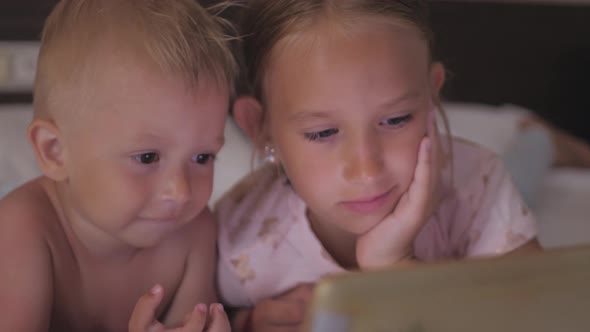 Two Kids in Bed Playing a Tablet in Social Internet in the Dark Light. Close Up of Little Boy and