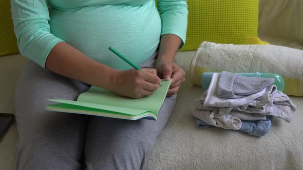 Cute Pregnant Woman Writing Packing List for Maternity Hospital With Notebook Prepares Bags