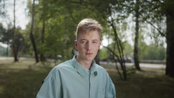 A Young White Disabled Man in the Wheelchair is Sitting in the Park and Looking at the Camera