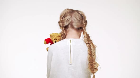 Sad Small Caucasian Girl with Long Blonde Hair Standing on White Background with Her Back to Camera