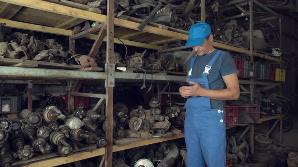 employee of auto disassembly, completes or checks car parts from tablet computer