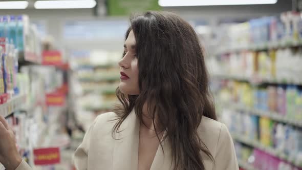 Portrait of Thoughtful Pretty Woman Examines Goods on the Supermarket Shelves