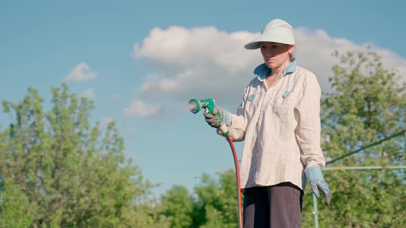 Woman Holding a Water Hose and Watering Beds or Plants in the Backyard