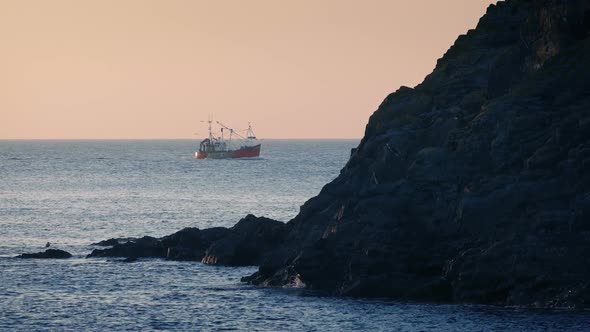 Fishing Boat Passes Behind Rocks At Sunset