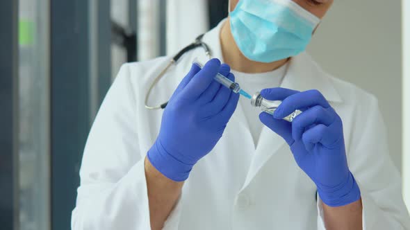 A Young Doctor in a Protective Mask Draws a Vaccine Into a Syringe