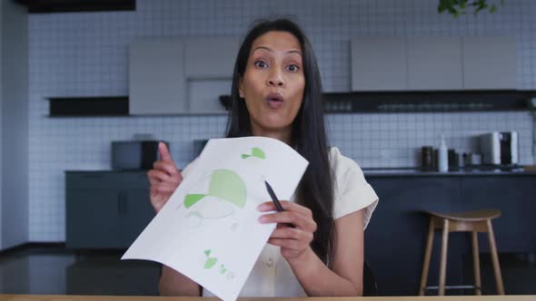 Mixed race businesswoman having video chat going through paperwork in office kitchen