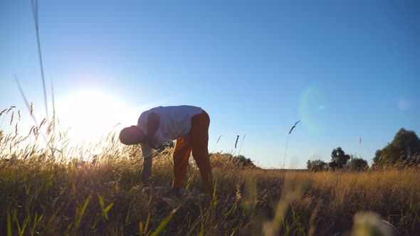 Young Man Practicing Yoga on Mat at the Field on a Sunny Day. Sporty Guy Doing Exercise at the
