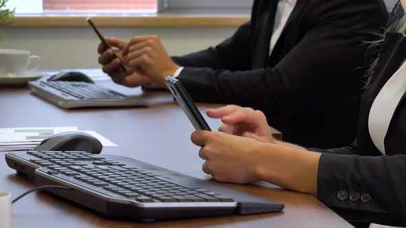 Two Office Workers, , Sits at Desks in Front of Computers and Work on Smartphones